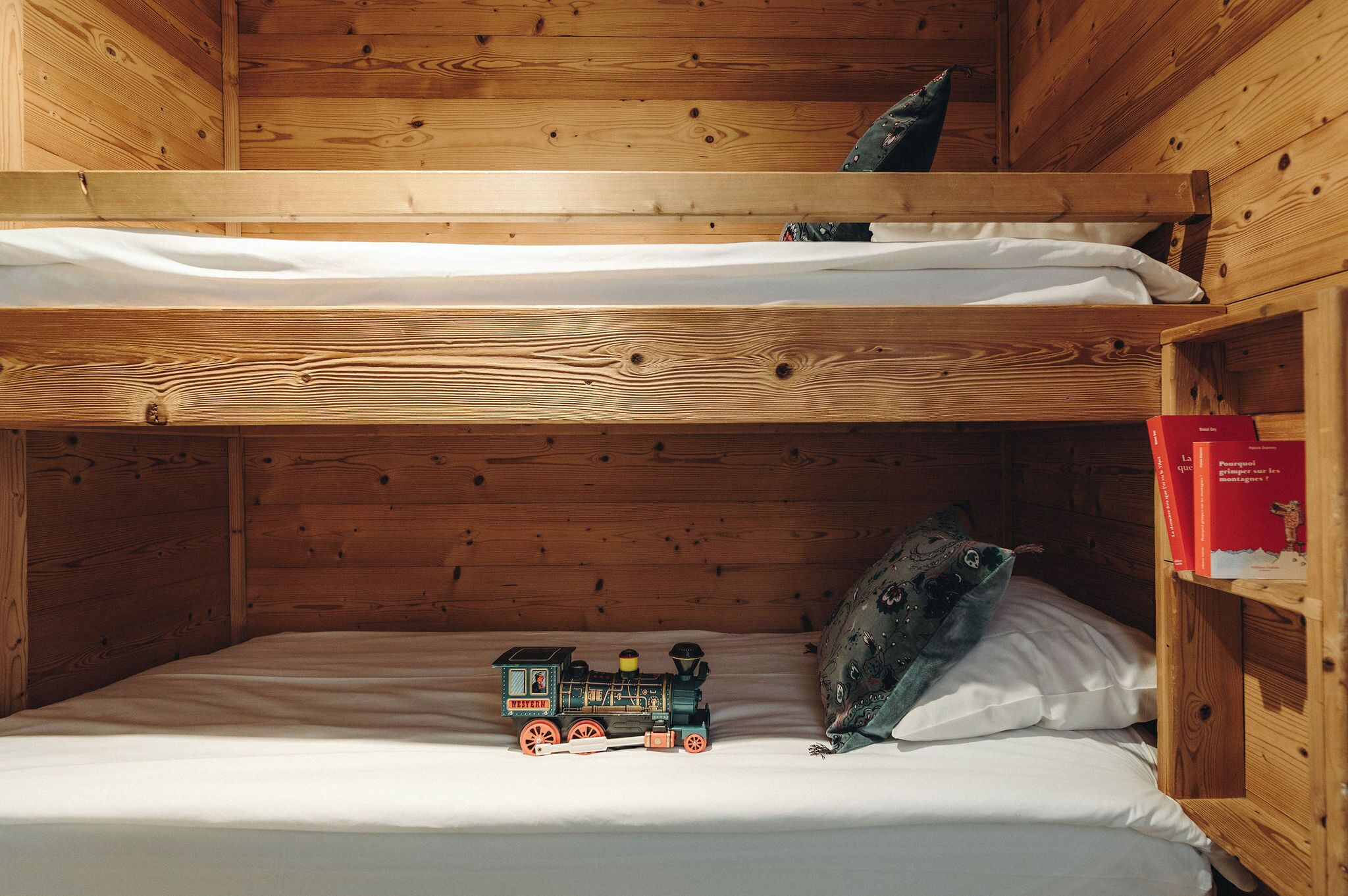 A bunk bed with a toy train on the lower bed and a bookshelf with books on the right.