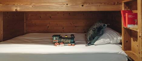 Una cama litera con un tren de juguete en la cama inferior y una estantería con libros a la derecha.