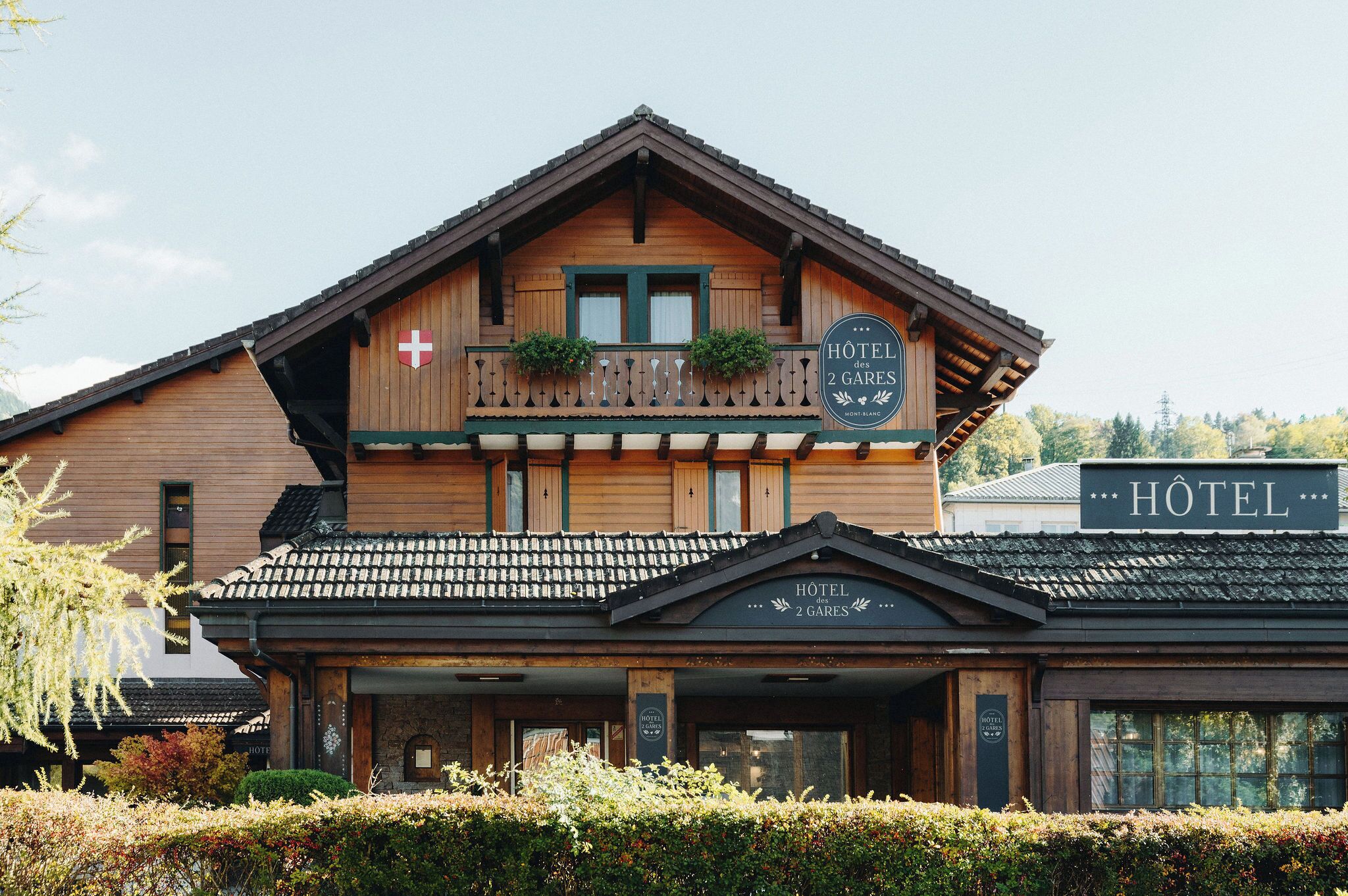 A wooden hotel with a balcony, a sign indicating it has 2 rooms, and a Swiss flag.