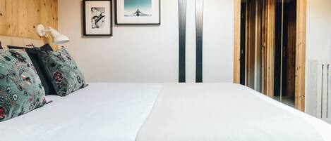 A hotel room with a wooden headboard, two framed pictures on the wall, and a pair of skis leaning against the wall.