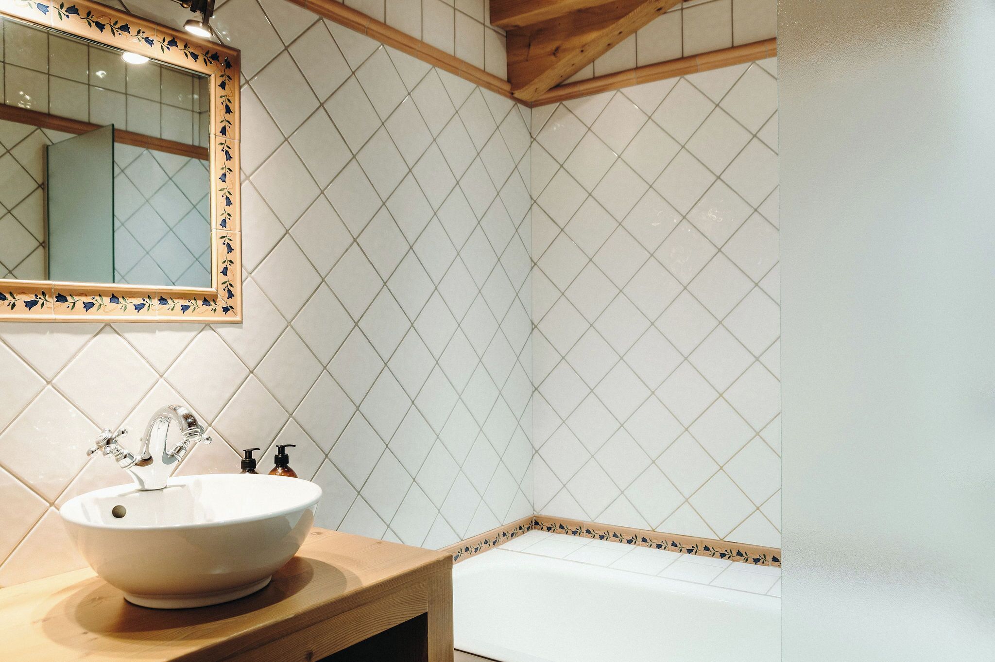 Un baño con lavamanos blanco, un espejo con marco decorativo y pared de azulejos.