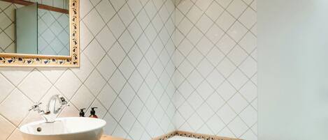Een badkamer met een witte wastafel, een spiegel met decoratieve lijst en een betegelde muur.