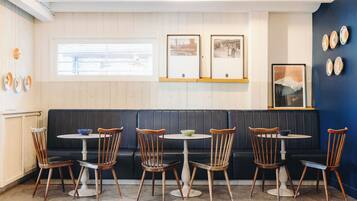 A restaurant interior with a dark-colored booth seating area, wooden chairs, and a small round table with a bowl.