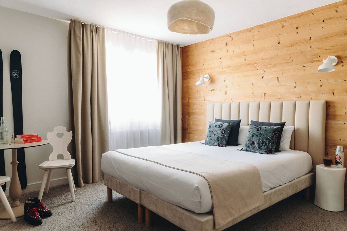 Une chambre d’hôtel avec un grand lit, un mur décoratif en bois, un bureau avec une chaise et une planche de ski appuyée contre le mur.