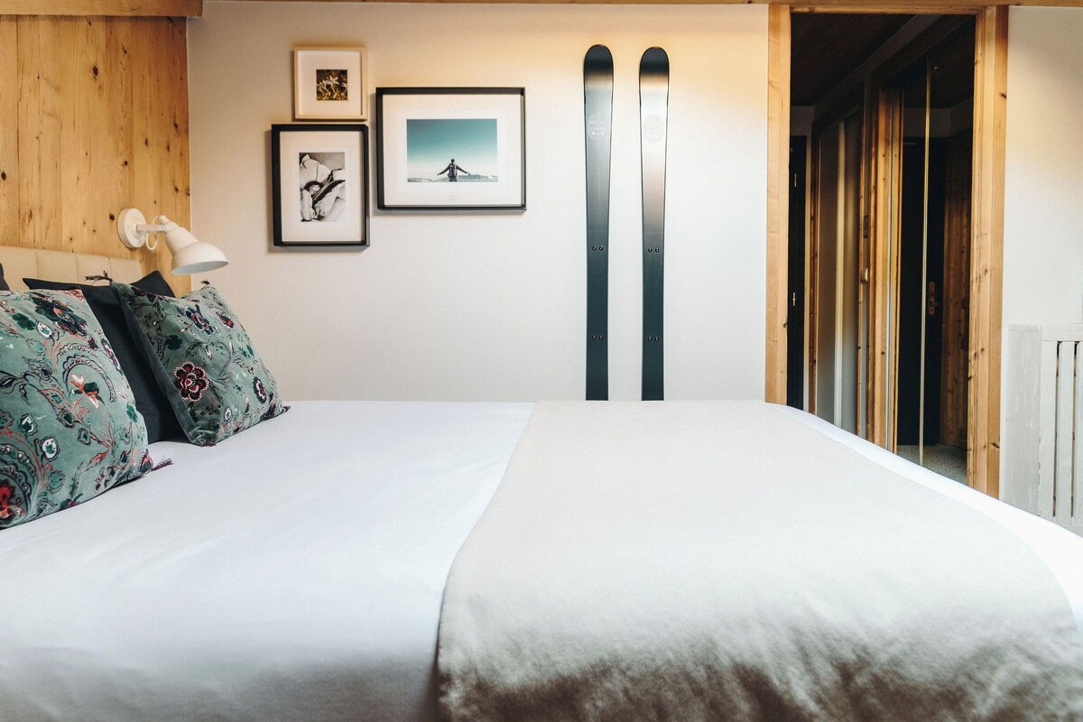 A hotel room with a wooden headboard, two framed pictures on the wall, and a pair of skis leaning against the wall.