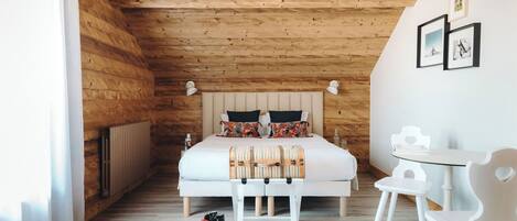 Un dormitorio con paneles de madera, una cama, mesitas de noche y una pequeña mesa con sillas.