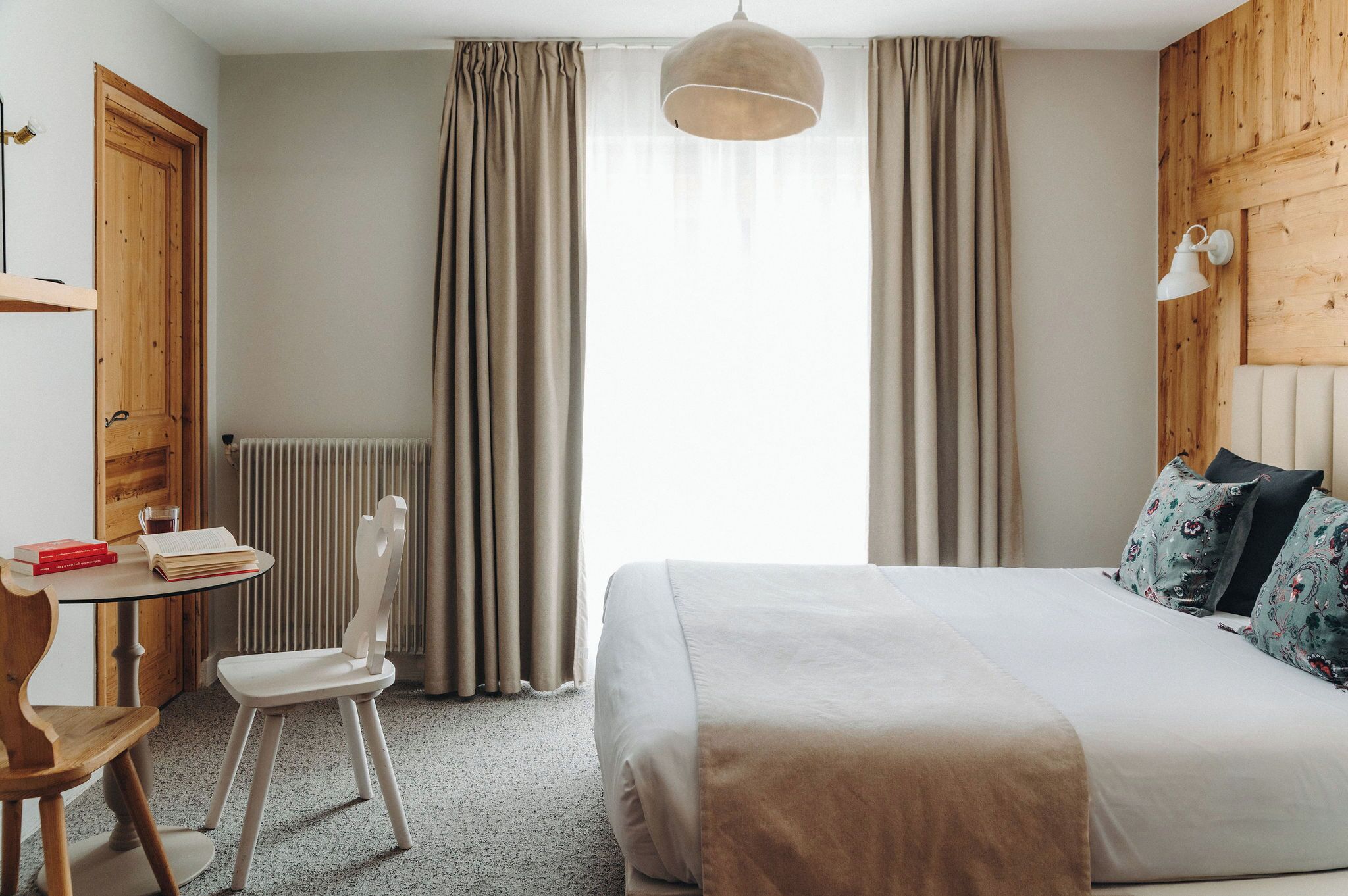 A bedroom with a bed, a chair, a table, and a window with curtains.