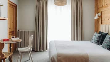 Un dormitorio con cama, una silla, una mesa y un ventanal con cortinas.