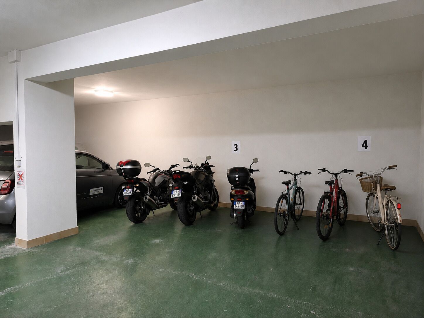Ett parkeringsgarage med motorcyklar och cyklar uppradade i rader, numrerade skyltar och en bil i bakgrunden.