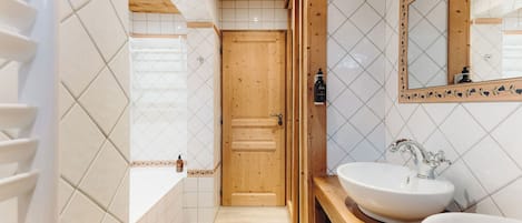 A bathroom with a wooden door, white tiled walls, a large mirror, and two sinks.