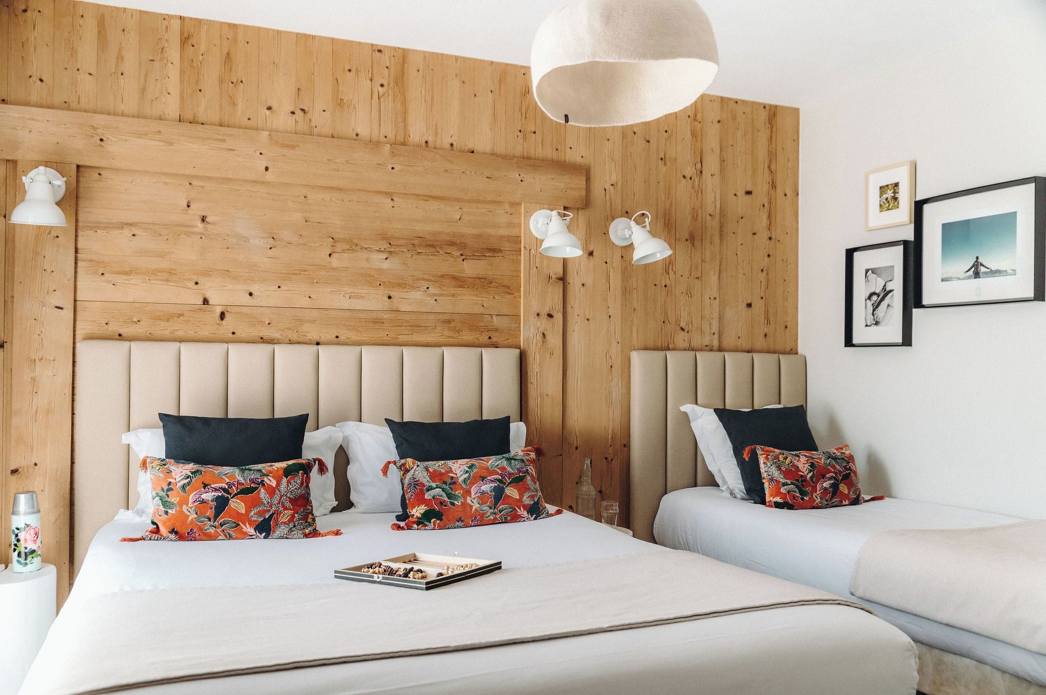 A bedroom with a wooden headboard, two bedside tables, a bed with floral pillows, and a hanging light fixture.