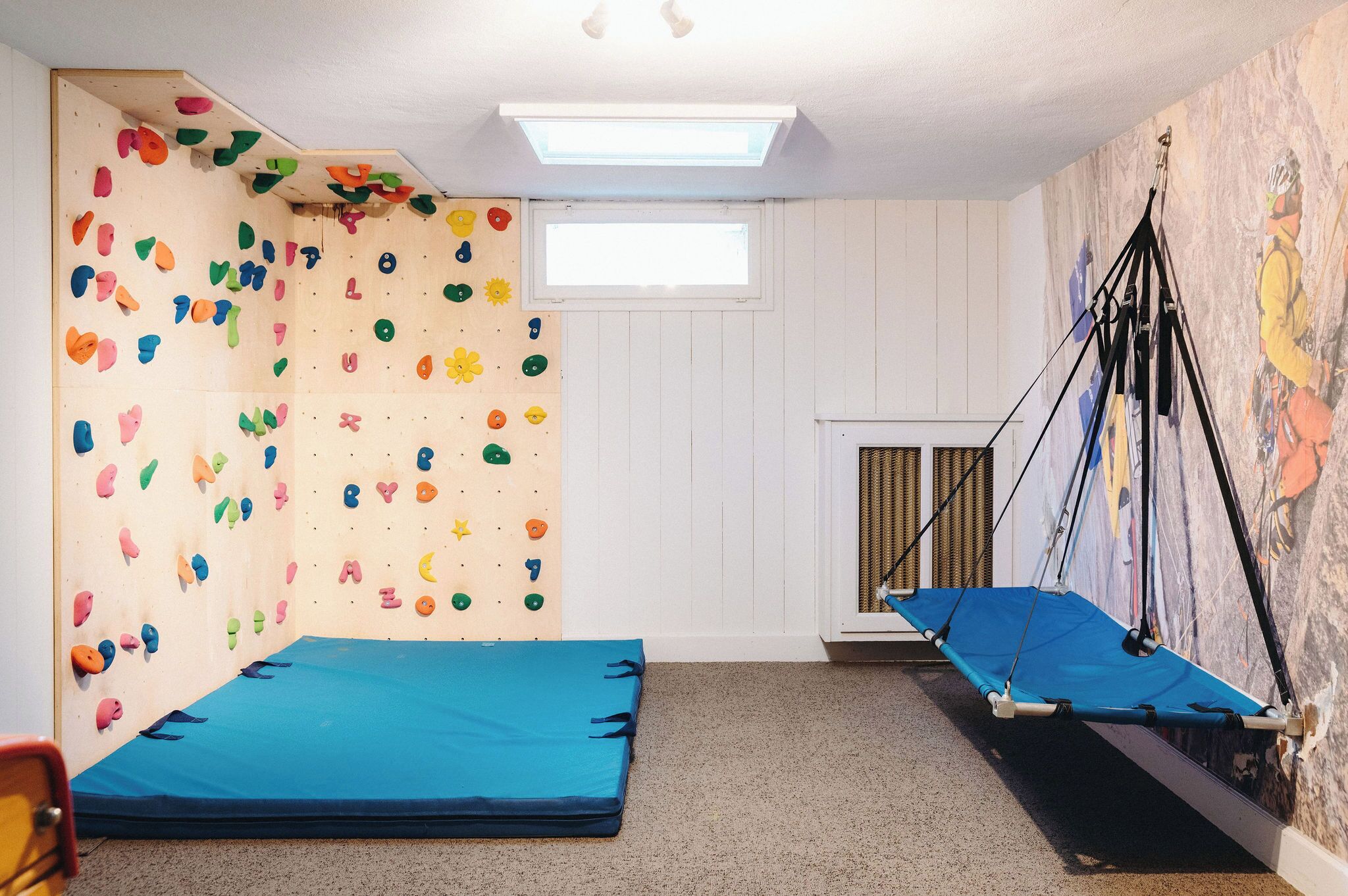 Una habitación con pared de escalada, una hamaca y un ventanal.