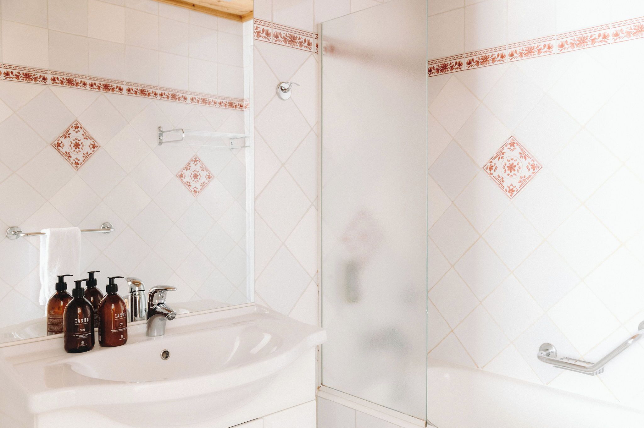 A bathroom with a white sink, three bottles of shampoo, a mirror, and a shower with a glass door.