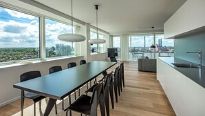 Cocina moderna con una isla grande y comedor, ventanas amplias con vista a la ciudad y un televisor de pantalla plana.