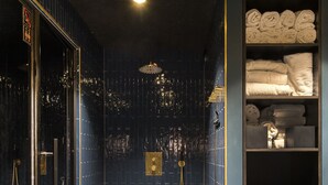 Un baño moderno con paredes de azulejos azul oscuro, una cabina de ducha de vidrio y un mueble de tocador de madera con toallas.