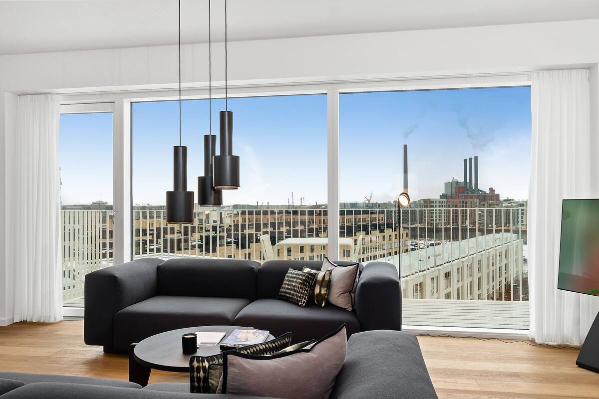 Una sala de estar moderna con un ventanal grande, un sofá negro, una mesa de centro y un televisor.
