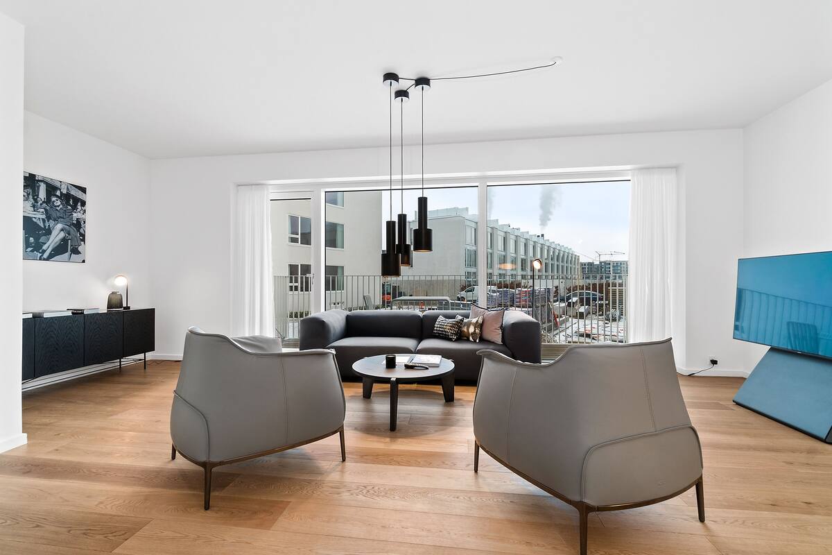 Una sala de estar moderna con un sofá, dos sillones, una mesa de centro y un televisor.