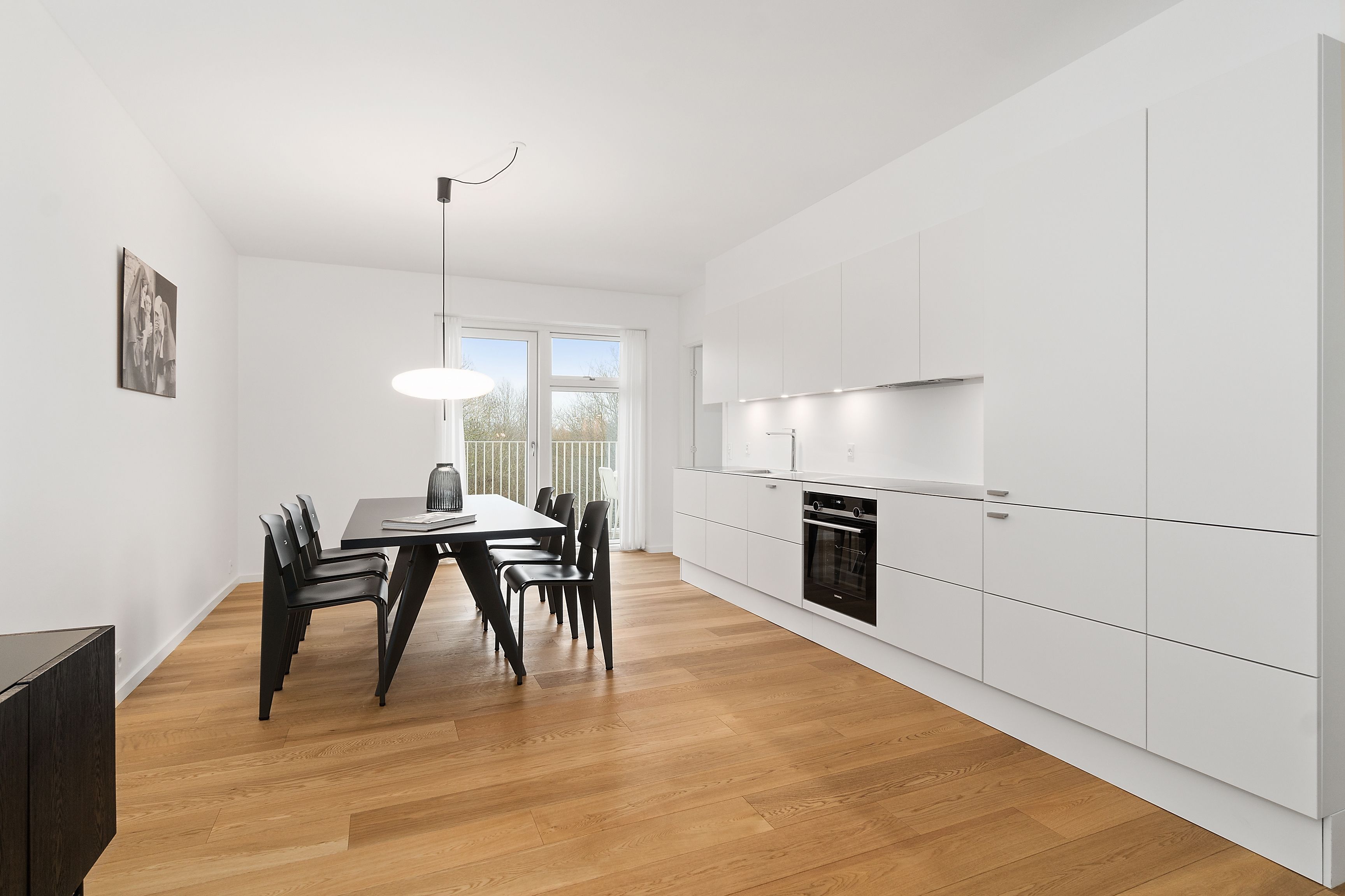 A modern kitchen with white cabinets, a dining area with a wooden table and chairs, and a pendant light.