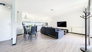 Een moderne woonkamer met een grijze bank, een eettafel met stoelen en een flatscreen televisie aan de wand.