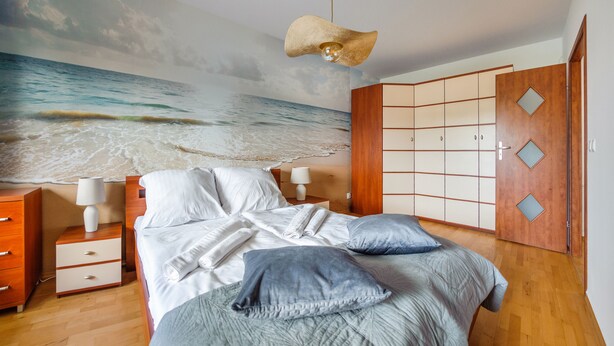 Een slaapkamer met een bed, nachtkastjes, een dressoir, een kledingkast en een strandreliëf op de muur.