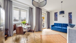 Een moderne woonkamer met een blauwe bank, een eettafel met stoelen en een keuken met een koelkast.
