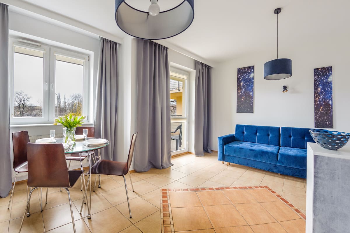 Een moderne woonkamer met een blauwe bank, een eettafel met stoelen en een keuken met een koelkast.