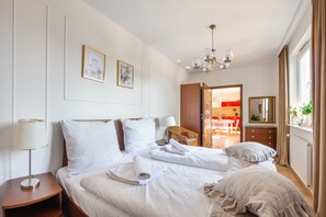 Une chambre d’hôtel avec un lit soigneusement fait, une table de chevet avec une lampe, un tableau accroché au mur et une vue sur la salle à manger adjacente.