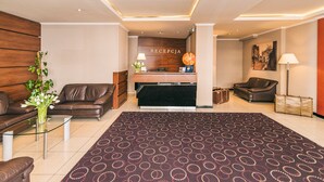 Un moderno vestíbulo de hotel con mostrador de recepción, sofás de cuero, alfombra estampada y una planta.