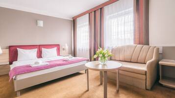 Una habitación de hotel con cama, sofá, una mesita y un jarrón de flores.