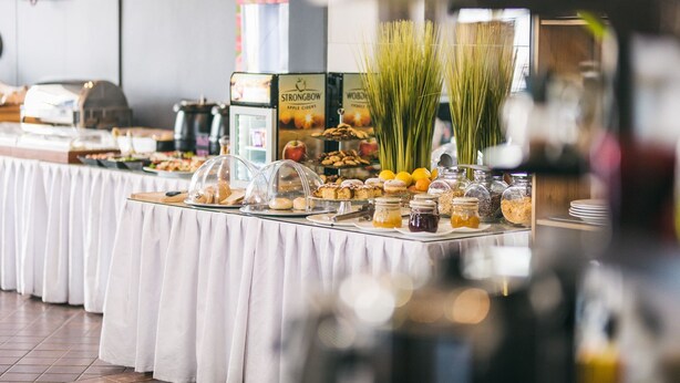 Una mesa de bufé con diversos alimentos y condimentos, incluyendo pasteles, frutas y frascos con salsas.