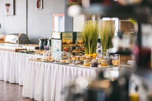 Una mesa de bufé con diversos alimentos y condimentos, incluyendo pasteles, frutas y frascos con salsas.