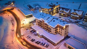 Un hotel cubierto de nieve con varias edificaciones, un estacionamiento y un telesilla al fondo.