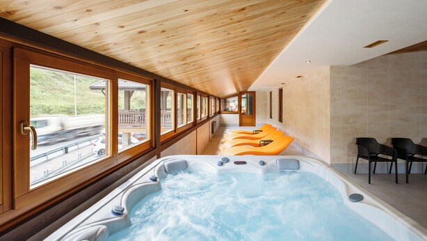 Un espacio de spa con un jacuzzi grande, techo de madera y asientos junto a las ventanas.
