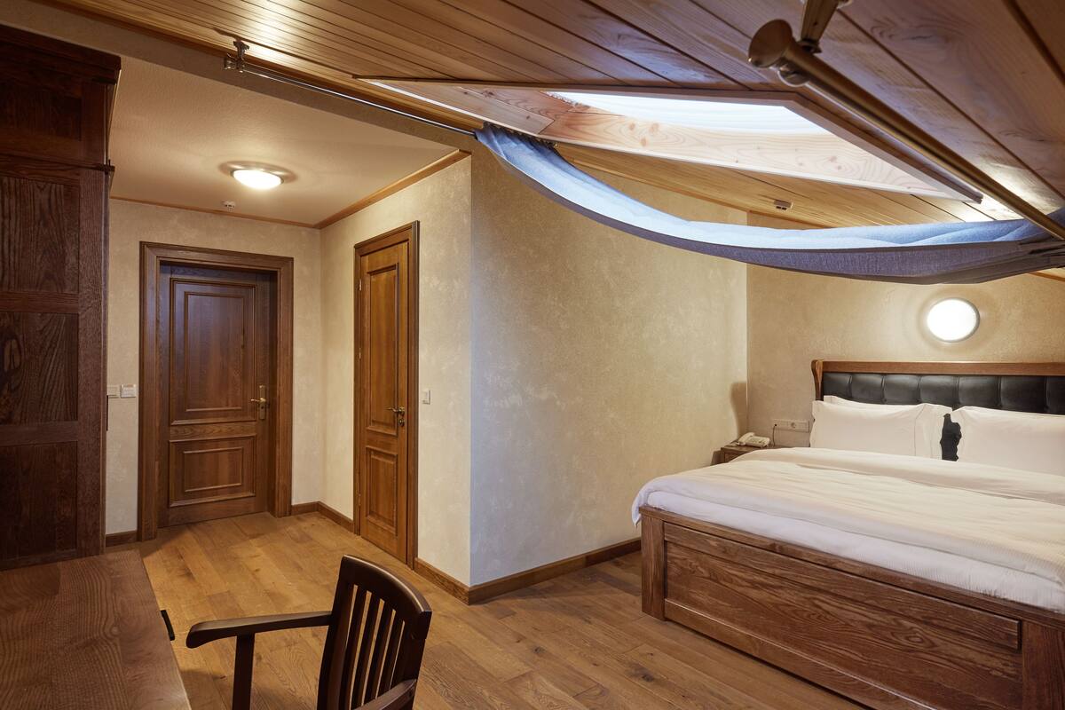 A bedroom with a wooden bed, a chair, a desk, and a wardrobe.