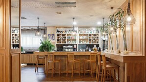 Zona de bar con taburetes de madera, estantes con botellas de licor y lámparas colgantes.