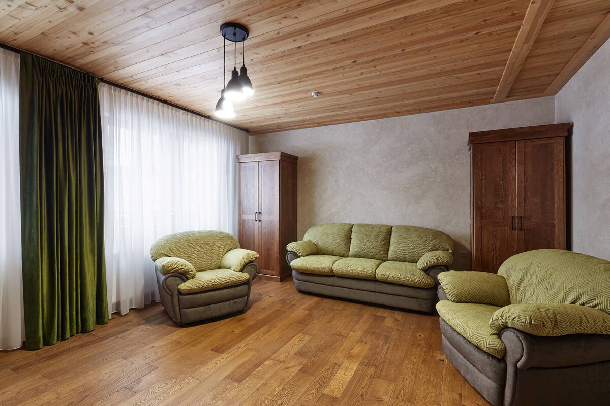 A living room with wooden flooring, a green armchair, a sofa, and a wooden wardrobe.