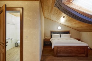 A bedroom with a wooden ceiling, a bed, a nightstand, and a view of the bathroom through an open door. - Ganz & SPA (Bukovel)
