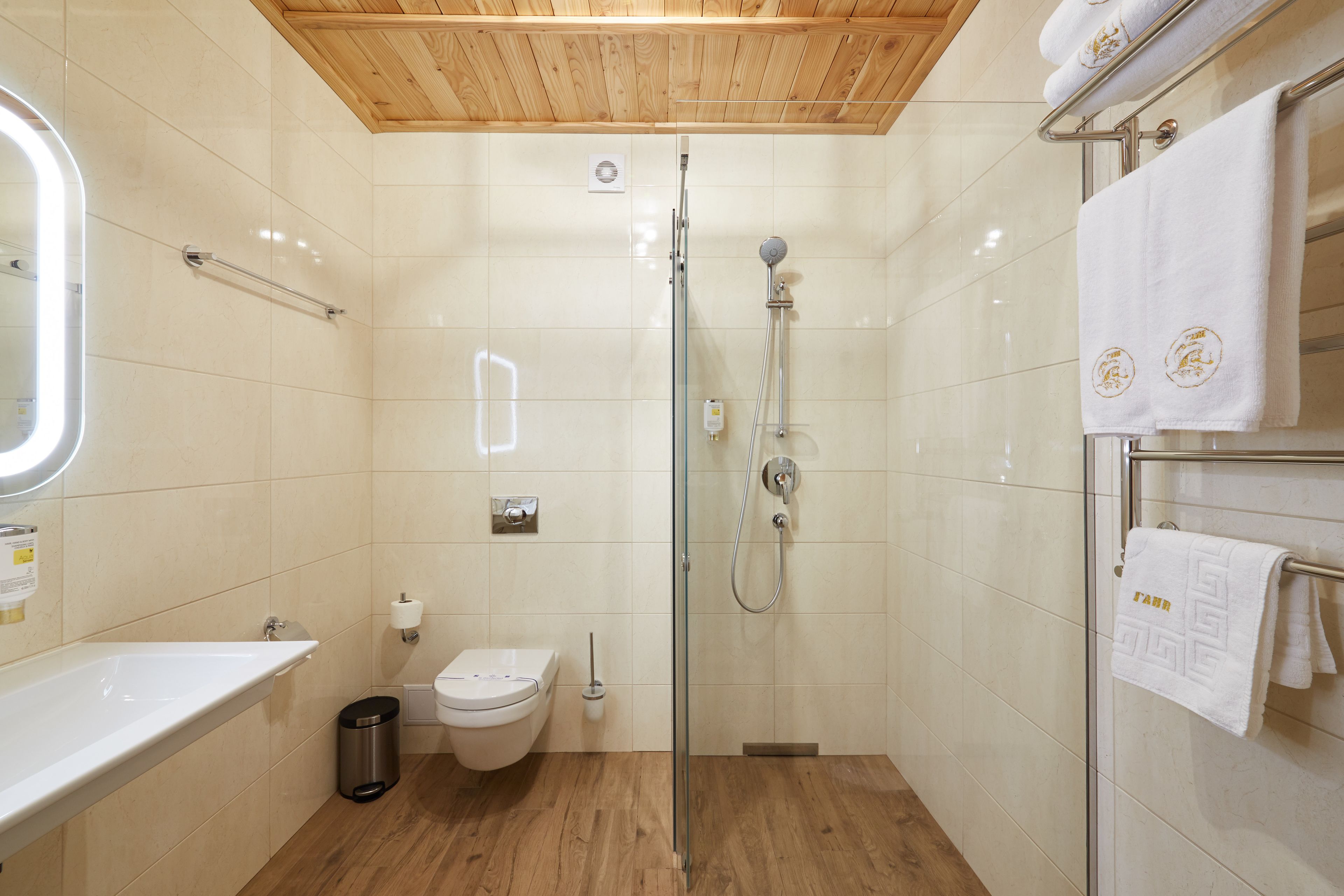 Un baño moderno con cabina de ducha de vidrio, techo de madera y lavamanos blanco.
