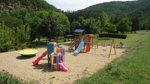 A playground with slides and climbing structures, surrounded by trees and hills. - Camping Le Roc Qui Parle (Nant)