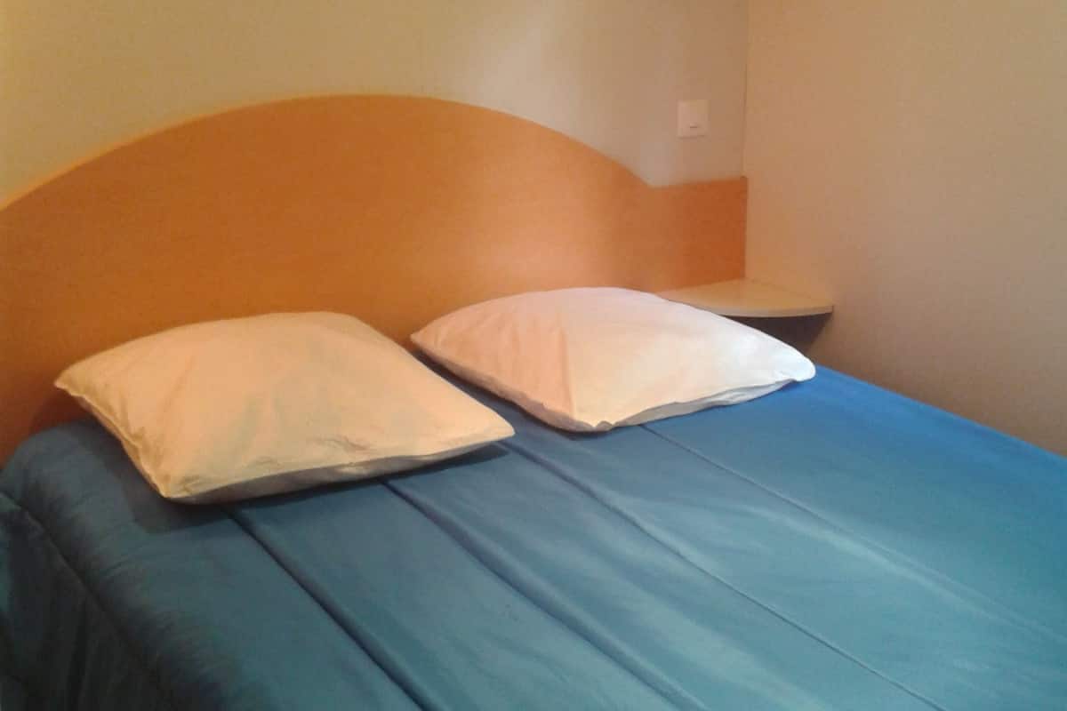 A bed with two pillows and a blue mattress in a room with a plain wall and a wooden headboard.