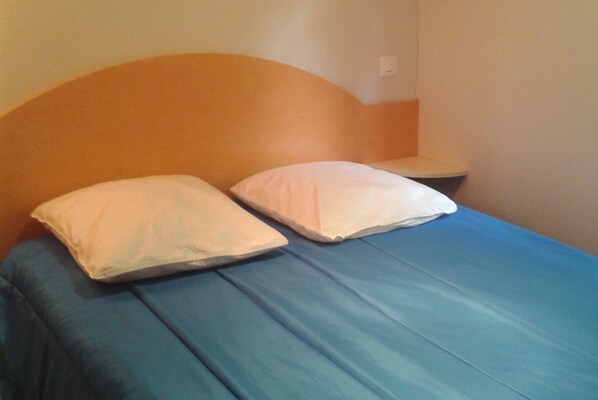 A bed with two pillows and a blue mattress in a room with a plain wall and a wooden headboard.
