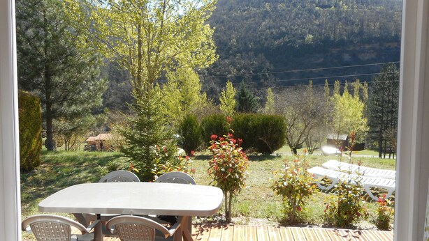 A patio with a table and chairs, surrounded by greenery and a view of a mountain. - Camping Le Roc Qui Parle (Nant)