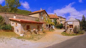 A stone building with a red-tiled roof, a reception area, and a stone wall. - Camping Le Roc Qui Parle (Nant)