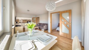 A modern dining area with a table set for four, a vase of white flowers, and a kitchen in the background. - Apartamenty Sun & Snow Olymp (Kolobrzeg)