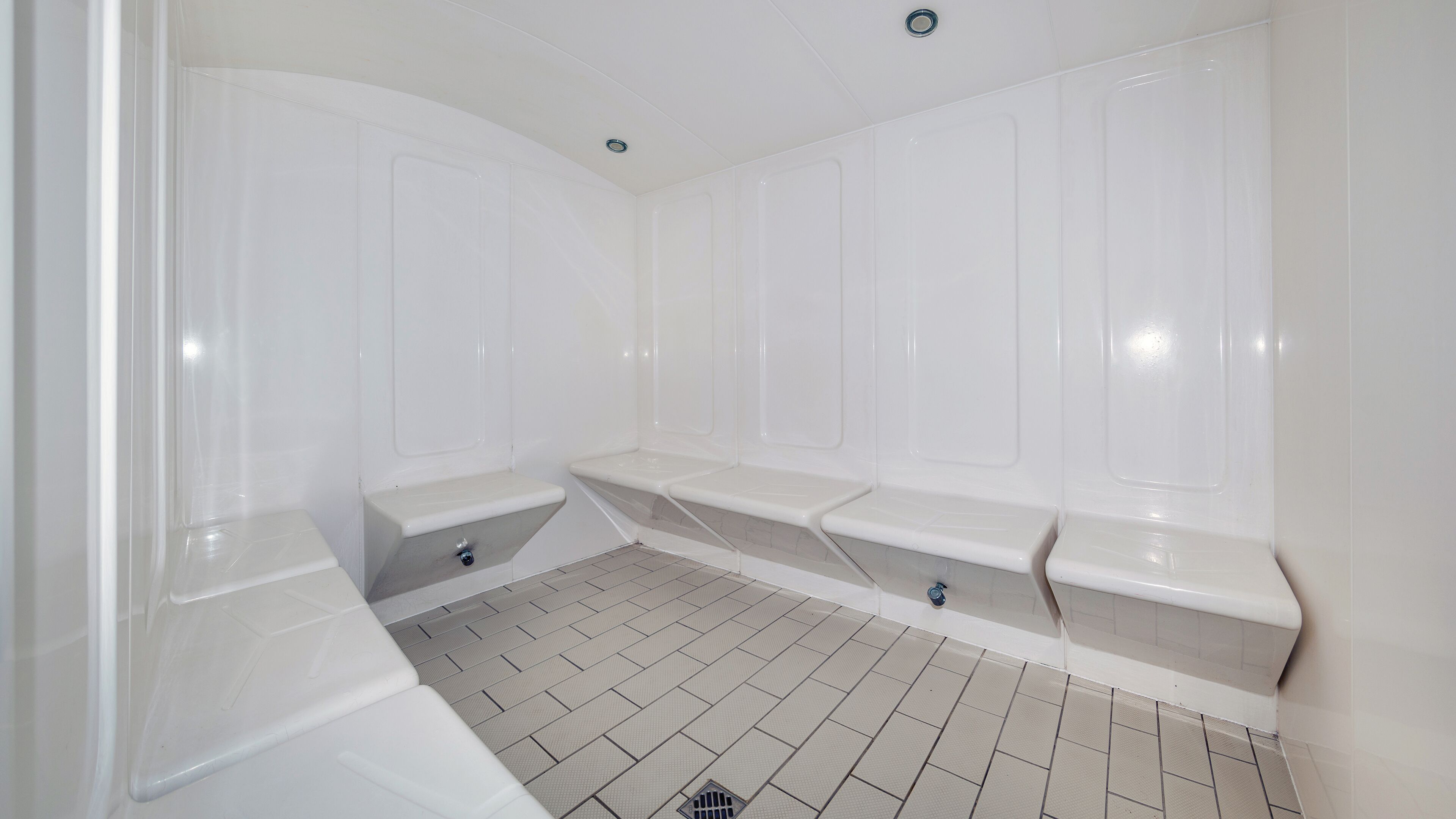 Un baño con paredes blancas, piso de baldosas y dos bancos.