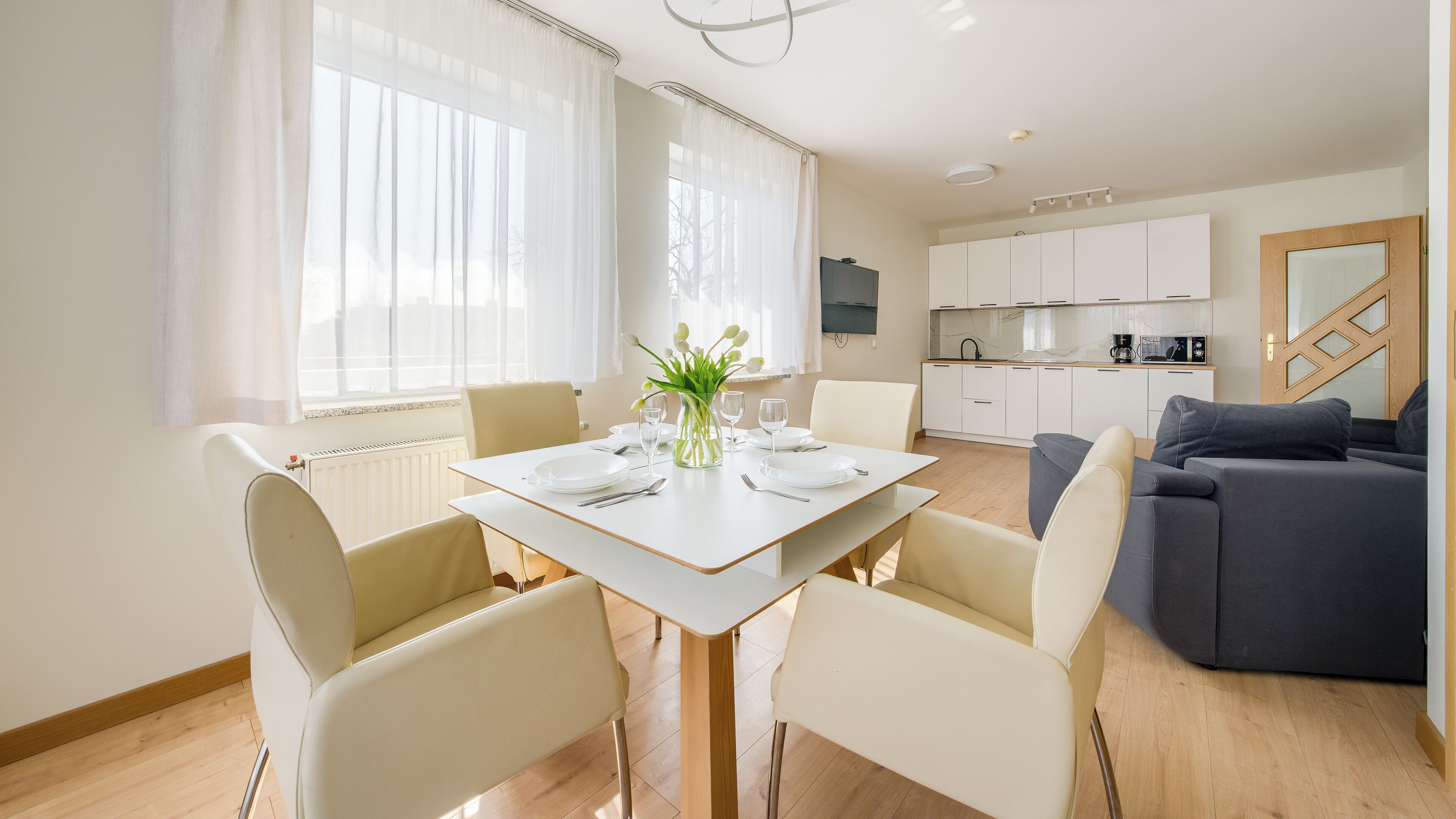 Une cuisine moderne avec des meubles blancs, une table à manger pour quatre personnes et un canapé dans l’espace salon.