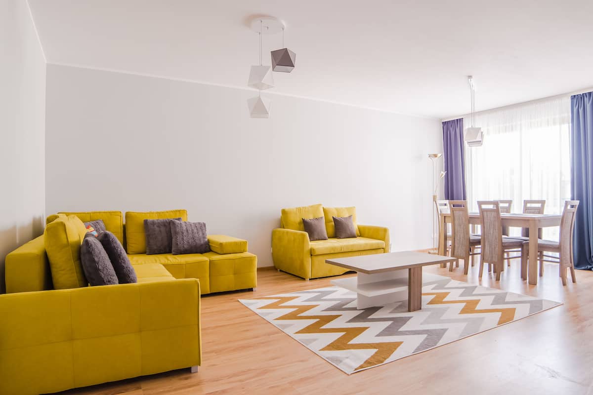 Una sala de estar moderna con dos sofás amarillos, una mesa de centro de madera y un comedor con mesa y sillas.