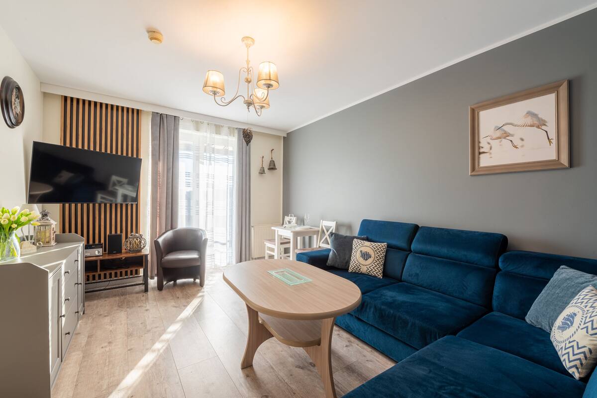 Una sala de estar moderna con un sofá azul, una mesa de centro de madera, un televisor y un comedor con una silla y una mesa.