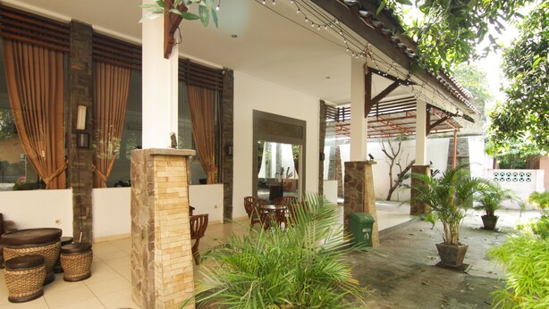 A covered outdoor area with stone pillars, wicker furniture, and potted plants. - Grand Ciwareng Inn (Purwakarta)