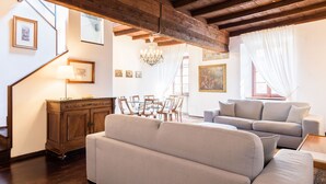 Uma sala de estar com teto de madeira, um sofá, uma mesa de jantar com cadeiras e um candelabro.